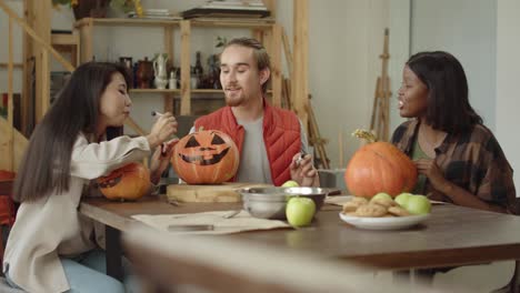 girls are looking how their friend is painting over a halloween pumpkin's face