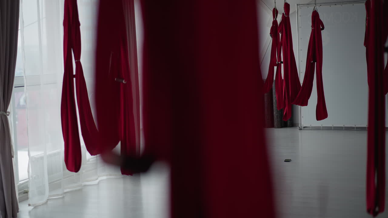 Fitness coach embraces partner standing barefoot on nail board inside tranquil aerial silk studio with flowing curtains and mirror wall conveying emotional support mindfulness trust
