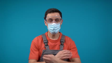 a construction worker wearing a face mask and safety goggles, with crossed arms against a blue background