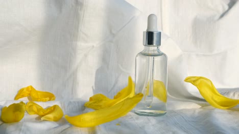 beautiful yellow flower petals and serum bottle on white fabric