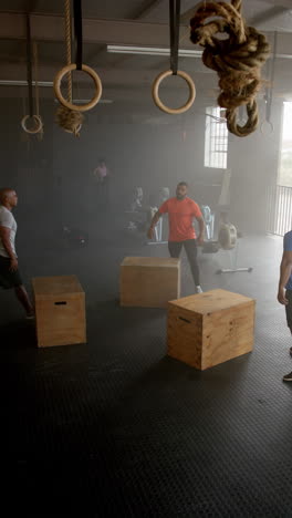 vertical video of diverse sports people jumping on boxes at gym in slow motion