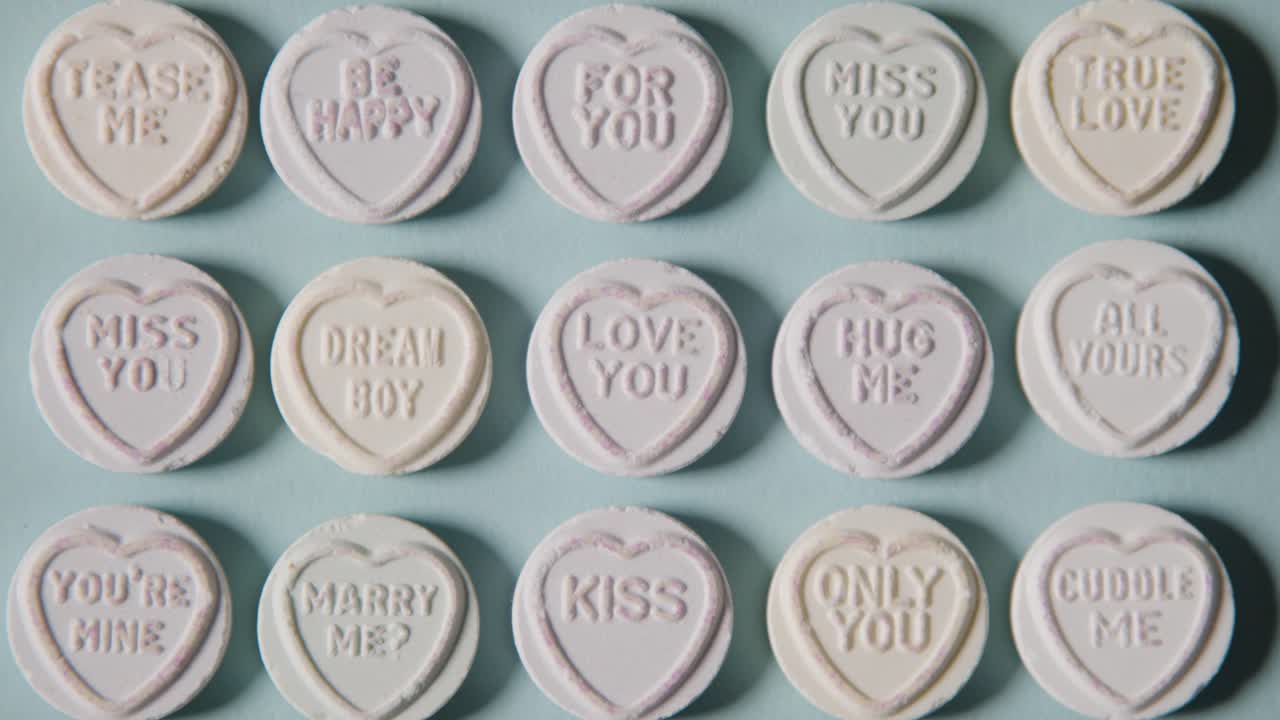 파란색 배경에 낭만적인 사랑의 메시지와 함께 심장 사탕을 휩쓸고 있는 사람의 전체 프레임 샷