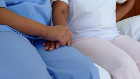 Front-view-of-female-doctor-holding-senior-woman-hand-on-bed-in-a-comfortable-home-4k