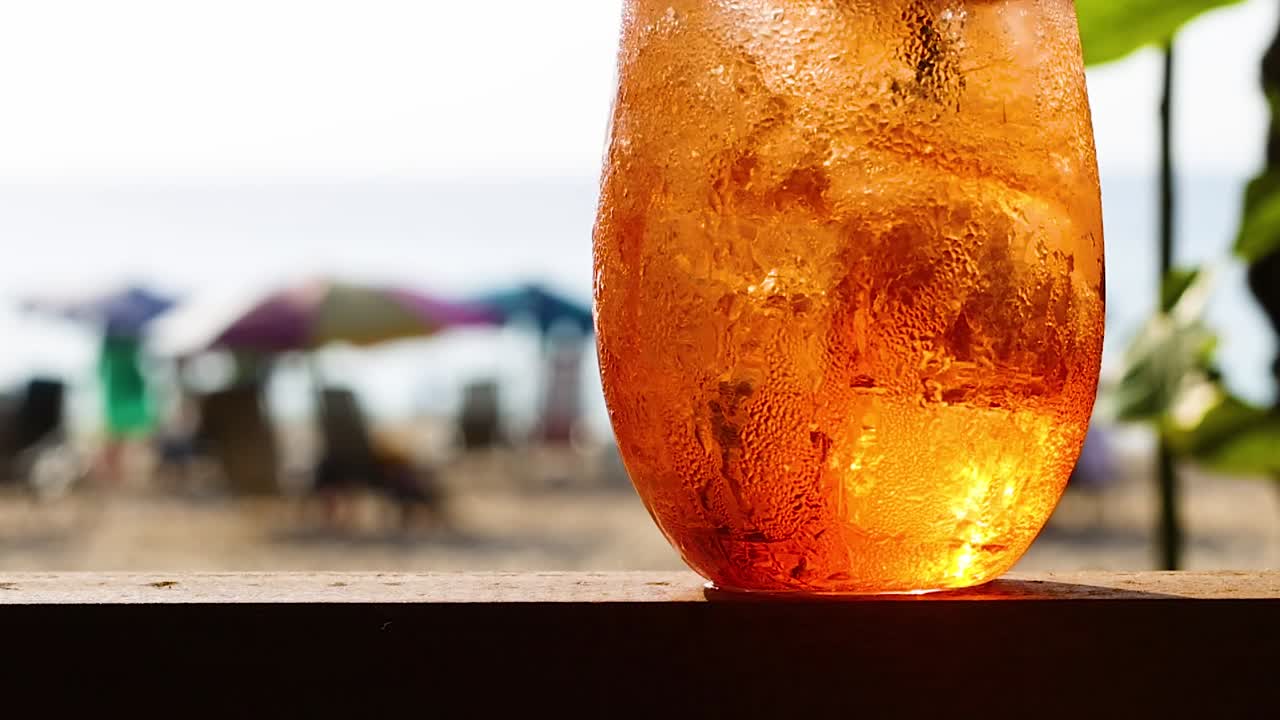 Close-up of a refreshing orange drink with ice, set against a backdrop of colorful beach umbrellas.