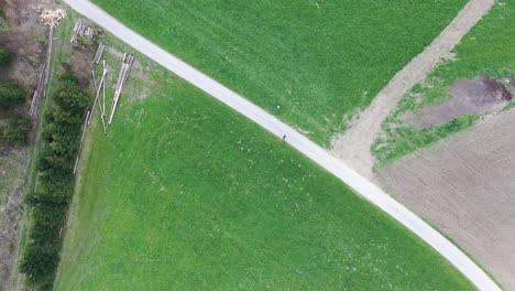 Two-people-walking-along-a-street-which-is-between-two-green-meadows