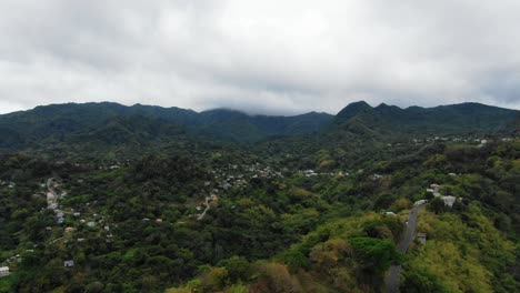 Lush-grenada-rainforest-with-scattered-homes,-cloudy-sky,-aerial-view