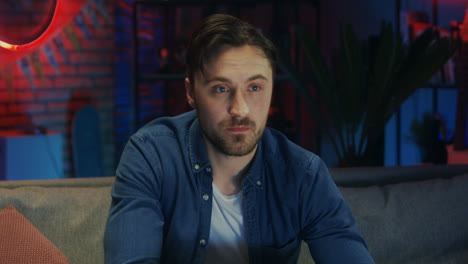 Portrait-Shot-Of-The-Good-Looking-Young-Guy-Sipping-Beer-From-A-Bottle-And-Watching-Tv-While-Changing-Channels-In-The-Dark-Living-Room-In-The-Evening