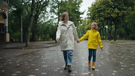 Happy-blonde-woman-walks-along-the-alley-with-her-teenage-daughter-in-a-yellow-jacket-and-talks-along-the-alley-in-the-park-with-a-dog-after-the-rain