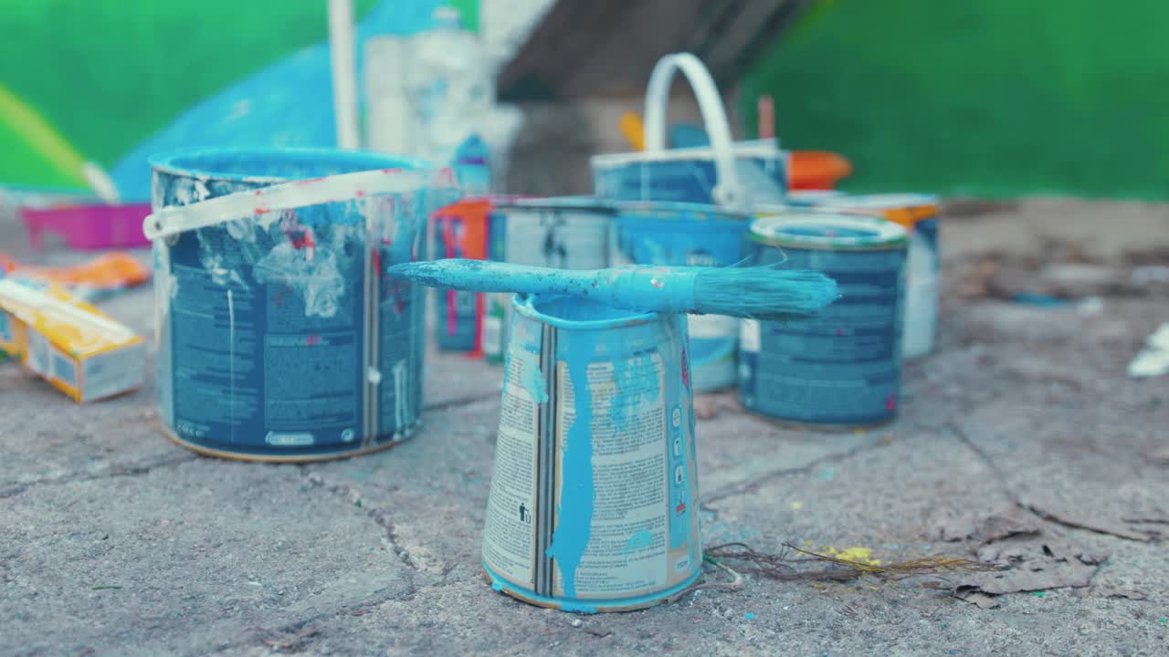 Brush with blue paint sits atop paint tins