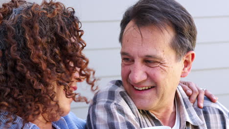 Portrait-Of-Smiling-Senior-Couple-Relaxing-Outside-Home-With-Hot-Drink