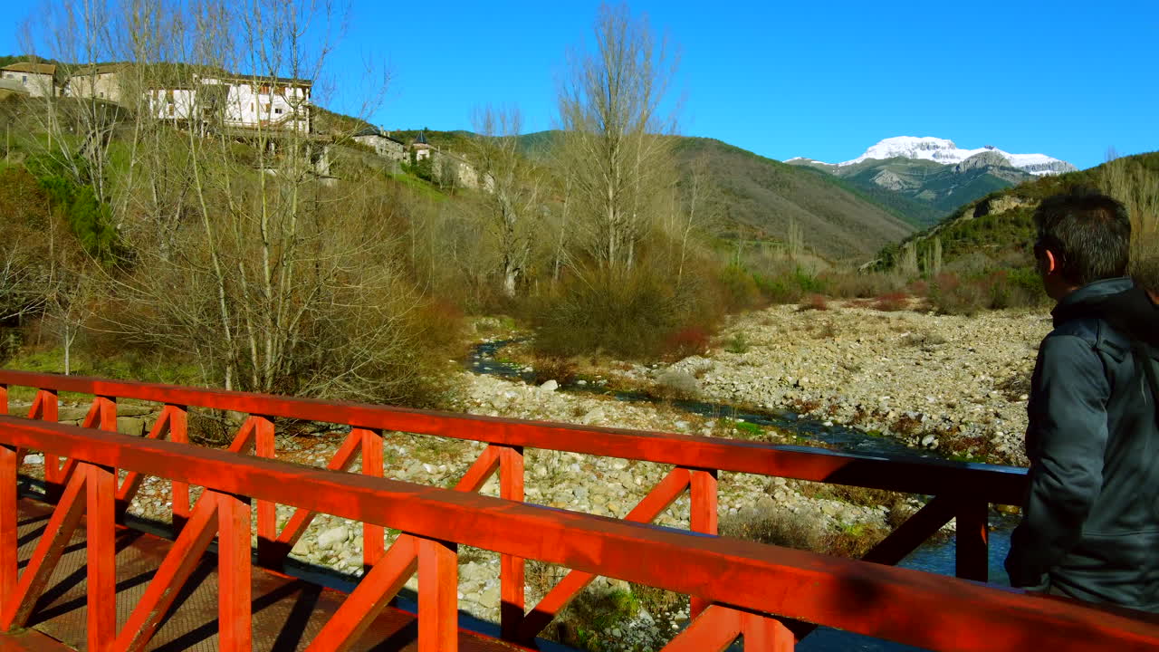 vista aérea de un hombre parado en un puente rojo de montaña contemplando el paisaje de los pirineos españoles