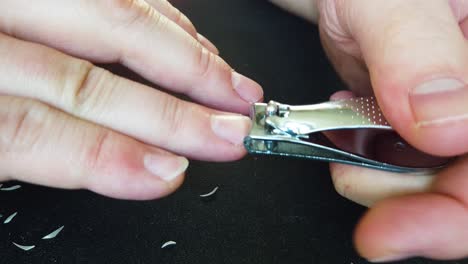 male clipping his finger nails against a black background with pile of nail clippings