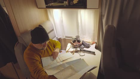 a man in a campervan sits at a table and unrolls a paper map