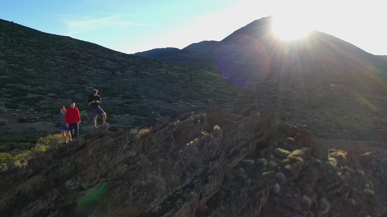 Hikers standing on a sharp rocky below the Pico de Teide mountain on Tenerife island watching the Sun setting behind the silhouette of the mountain. Hikers watching a sunset on Canary Islands in 4K