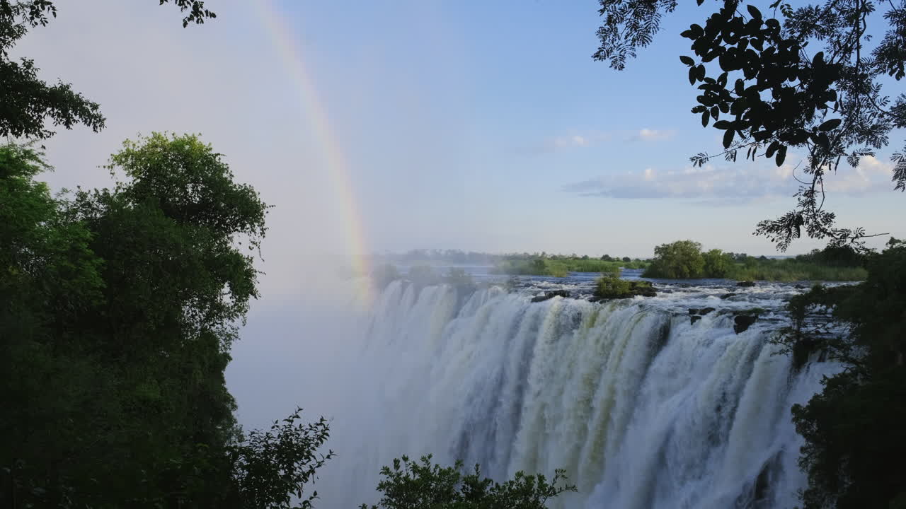 video estático de la parte superior de una cascada gigante con un arco iris bajando a través de la niebla