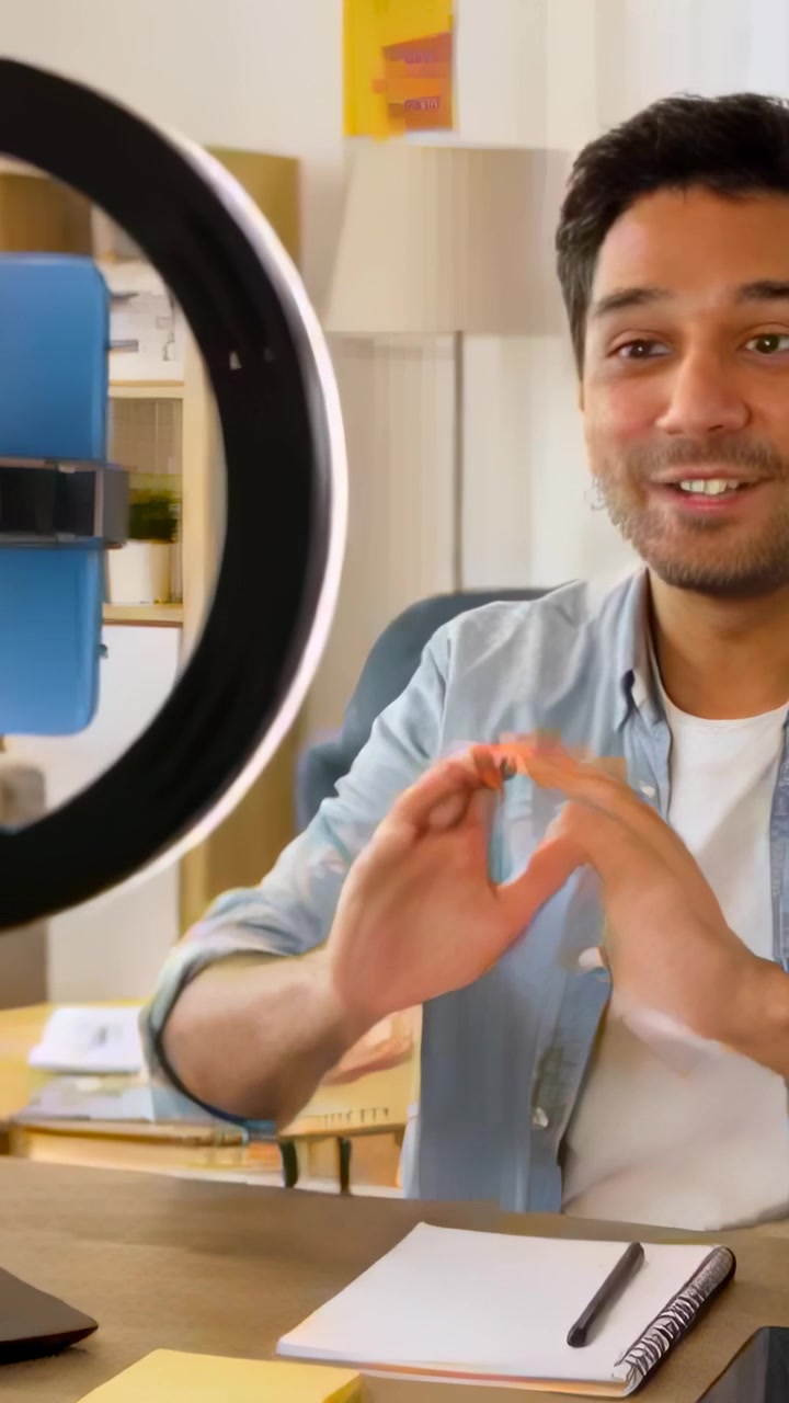 Video Vertikal: Merekam Pria Berkaus Biru Mempresentasikan Ide Sambil Memberi Isyarat di Rumah dengan Ponsel Ring Light