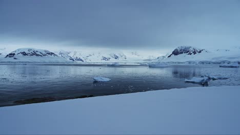 Antarctica-Mainland-Coastal-Scenery-on-Coast,-Winter-Landscape-with-Snow-Ocean-and-Mountains,-Icebergs-in-Sea-in-Beautiful-Dramatic-Dark-Moody-Blue-Seascape-on-Antarctic-Peninsula