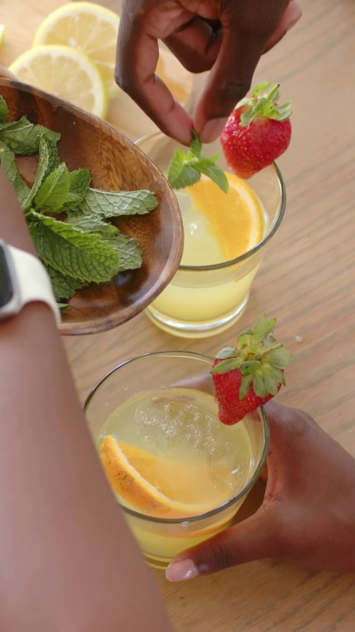 Vertical video: Moving mint bowl in frame, hands adding mint to drinks at table to present