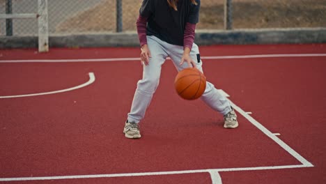 close-up a blonde girl with a bob hairstyle in a blue hat in a sports uniform hits an orange basketball ball from the red floor on a street court during her workout during the day