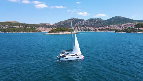 Barco-Solitario-En-La-Bahía-Cerca-De-La-Ciudad-Costera-De-Croacia-Contra-El-Fondo-De-Cielo-Azul-Y-Agua-Azul-Transparente-Y-Casas-Con-Techos-Rojos