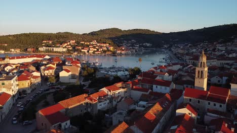 Drone-over-old-village-with-church-moves-cinematic-slowly-forward-towards-the-bay-with-sailboats-and-yachts