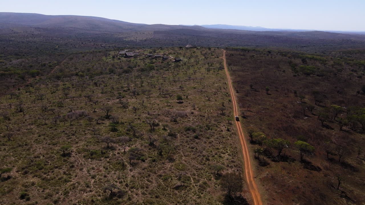 Ariel drone shot of a safari vehicle driving down a dirt road showing one fire-burnt area and an unburnt area in the winter months of Africa searching for wild animals