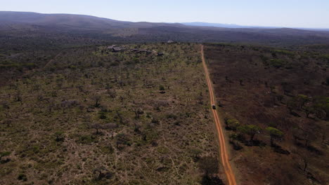 Ariel-Drohnenaufnahme-Eines-Safari-Fahrzeugs,-Das-Eine-Unbefestigte-Straße-Hinunterfährt-Und-In-Den-Wintermonaten-Afrikas-Auf-Der-Suche-Nach-Wilden-Tieren-Ein-Durch-Feuer-Verbranntes-Gebiet-Und-Ein-Unverbranntes-Gebiet-Zeigt