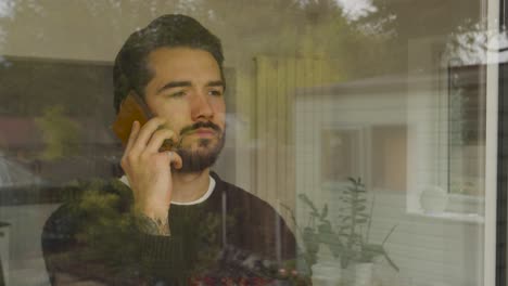 hombre mirando por una ventana hablando por un teléfono inteligente