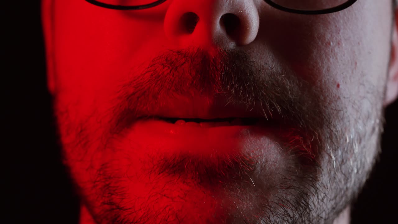A close-up of a man’s face under dramatic red lighting shows him biting his lip slightly, symbolizing tension, anticipation, or inner conflict in a cinematic moment