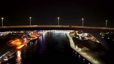 Die-Königin-Juliana-Brücke-Wird-Nachts-Beleuchtet,-Während-Die-Drohne-über-Die-Handelskade-Steigt