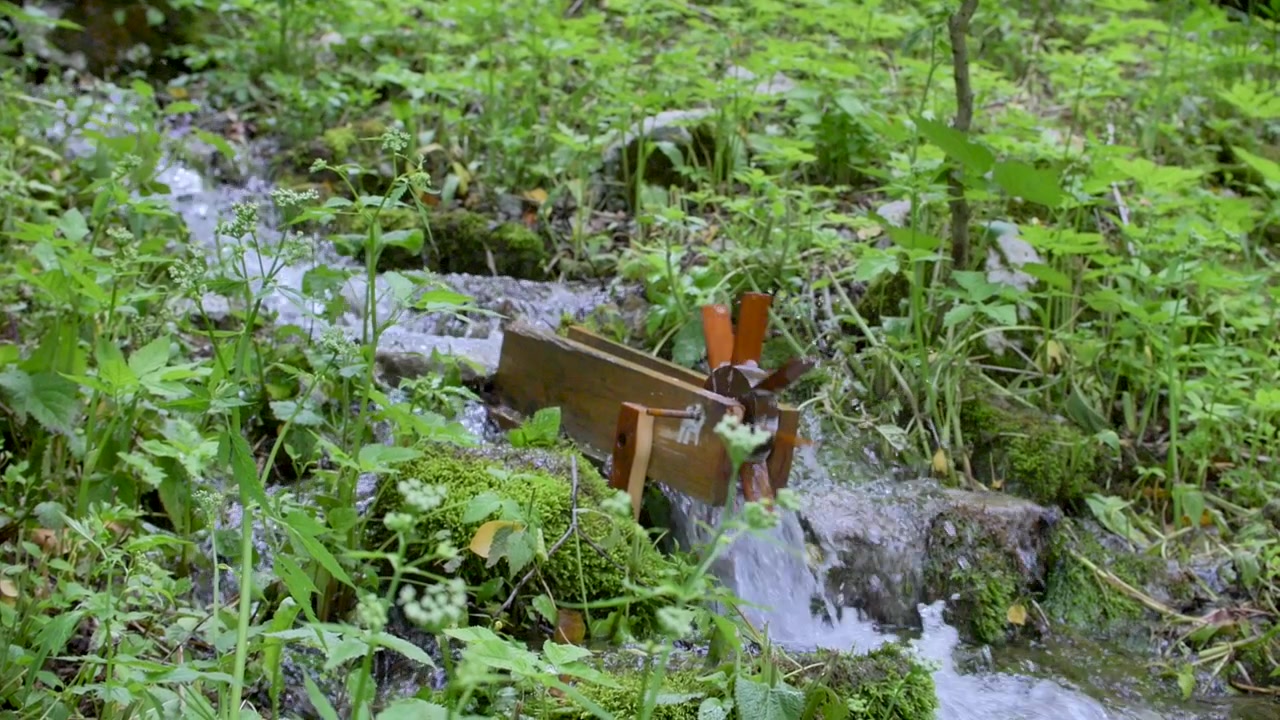 Petit moulin à eau en bois tournant sur un petit ruisseau en contrebas de la colline dans le sous-bois verdoyant. Roue à aubes au centre du cadre