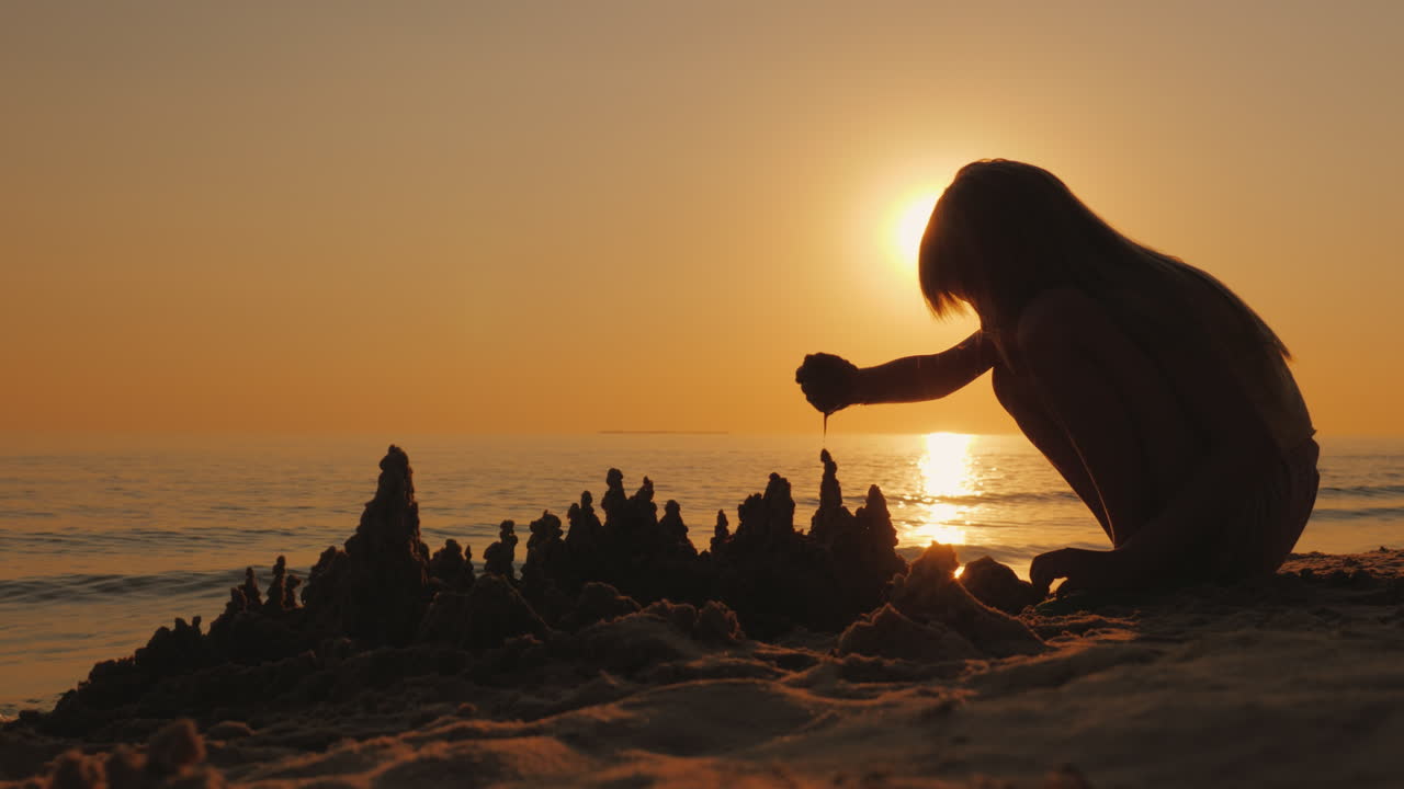 소녀는 바다 옆 모래에서 놀고 젖은 모래 4k 비디오의 아름다운 성을 짓습니다.