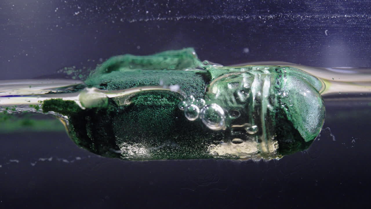 Pill dissolving in liquid, close-up view showing bubbles and green particles