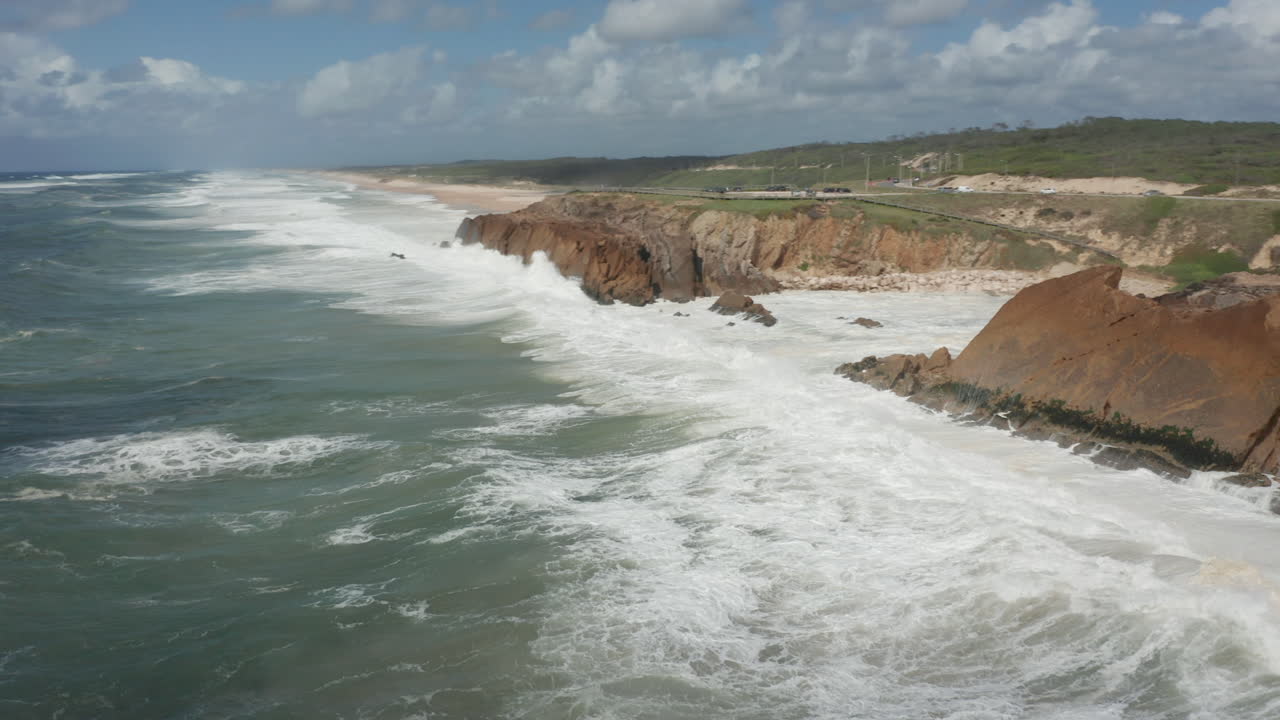 Aerial of a wild sea slamming into cliffs and flowing into a small bay
