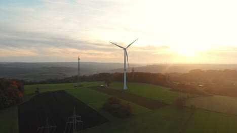 Vuelo-De-Drones-Sobre-Campos-Verdes-Con-Turbinas-De-Viento-Hacia-El-Amanecer