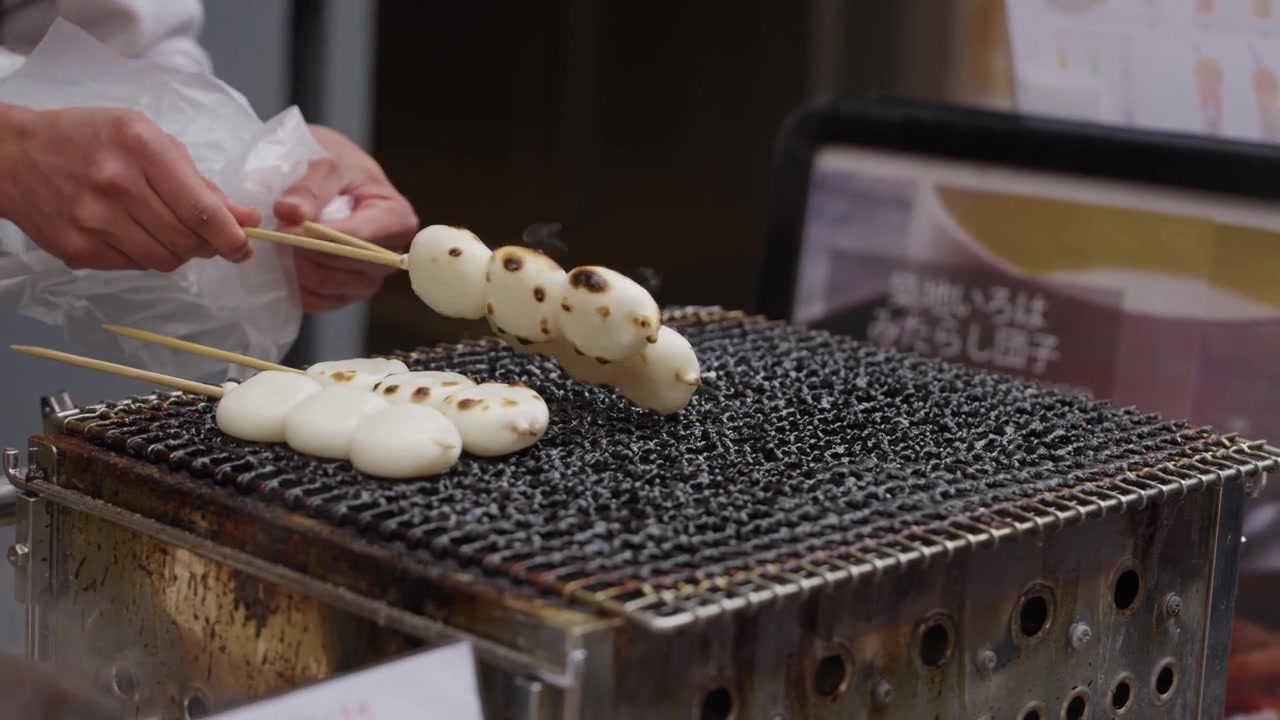 Açık hava Tokyo pazarında bir satıcı, kömür ızgarasında dango pirinç köftesi şişlerini pişiriyor.