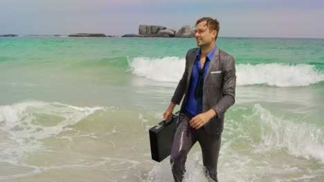 Front-view-of-Caucasian-Businessman-walking-with-briefcase-in-the-sea-at-beach-4k