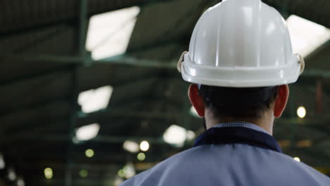 vista trasera del trabajador de fábrica masculino con casco y gafas caminando en una gran fábrica