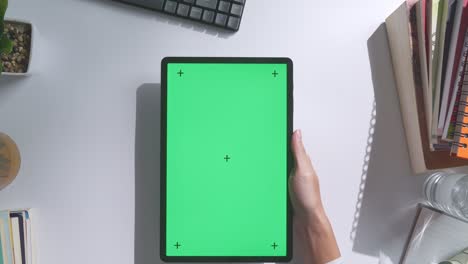 vista de arriba hacia abajo de una computadora portátil con pantalla verde simulada pantalla chromakey en un escritorio de oficina de madera al lado de la libreta con bolígrafos, gafas y un vaso de agua.