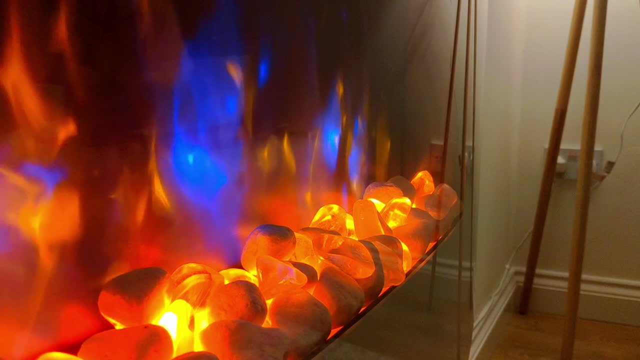 acogedora casa con chimenea eléctrica con rocas y llamas detrás de un cristal y patas de lámpara de pie vistas al fondo