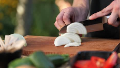 young man chops onions on a wooden board in his garden close up