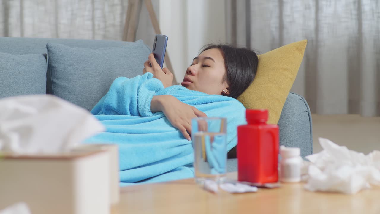 병든 여자 가 전화 와 약 을 가지고 소파 에 쉬고 있다