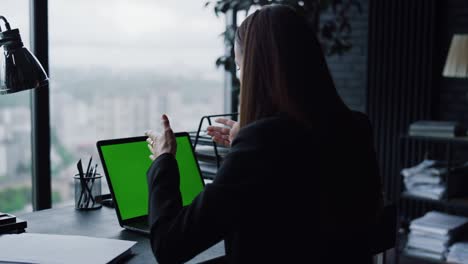 joven empresaria que usa una computadora portátil con pantalla verde para una llamada de video en la oficina en el hogar
