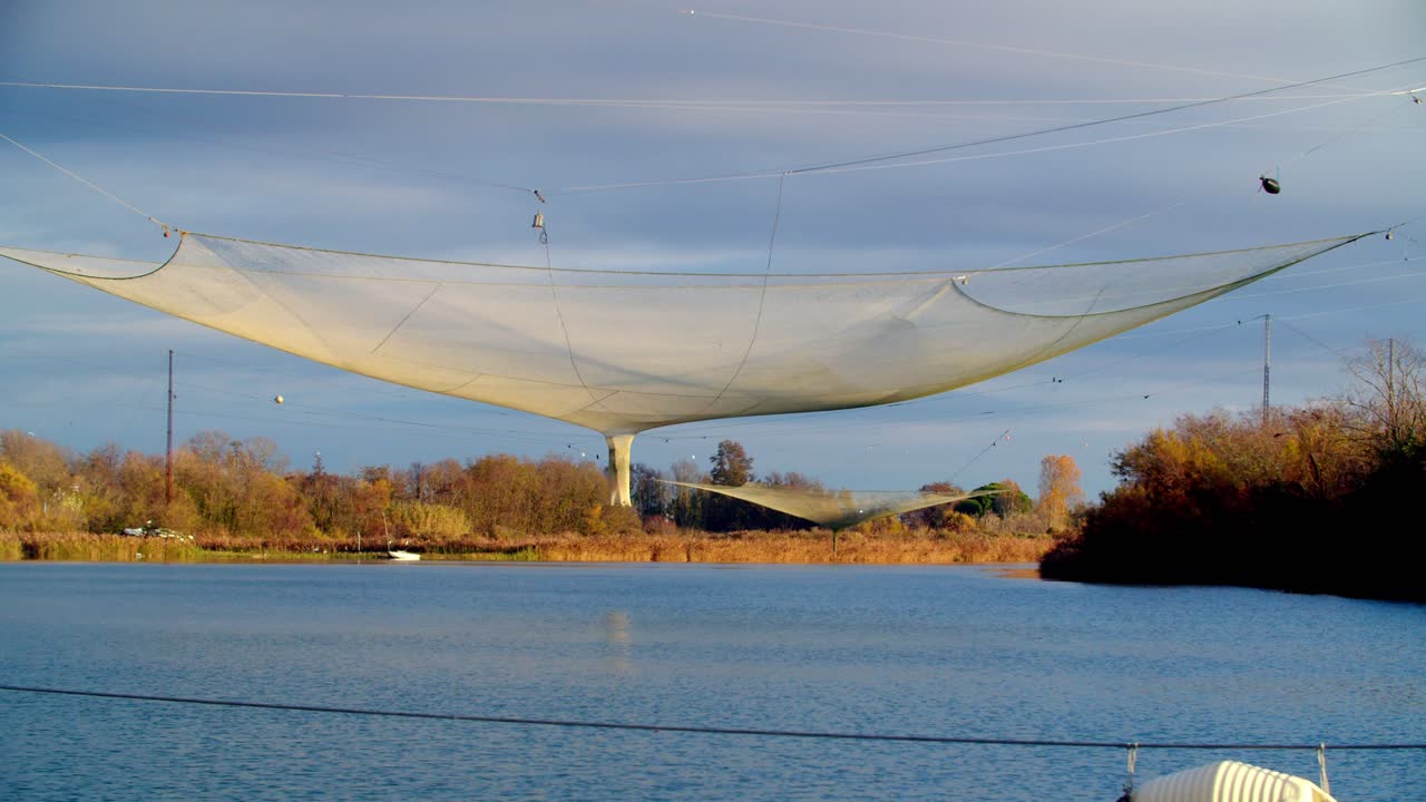 traditional fishing net on the Piave River at sunrise. Scenic landscape showing lush cultivated farm fields lining the riverbanks near Jesolo, Italy