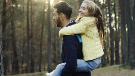 Un-Apuesto-Hombre-Caucásico-Haciendo-Girar-A-Su-Linda-Hija-En-La-Espalda-Mientras-Ella-Cierra-Los-Ojos-En-El-Bosque