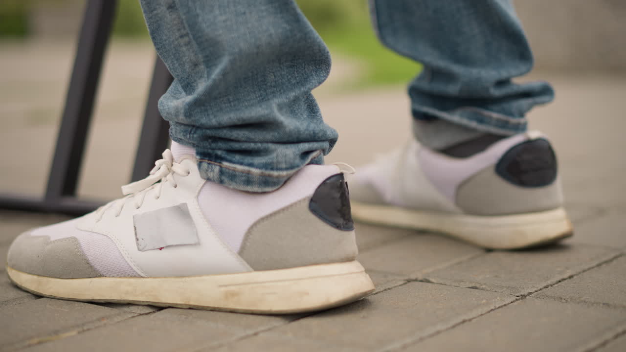 Nærbillede af sneaker der træder på flisebelagt fortov, denimmanchet over træningssko, fod aktiverer effektpedal nær stativ, rytmisk test til live-sæt, pulserende tempo og livlig urban energi fanget til musik.