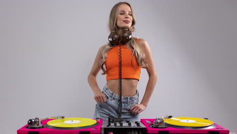 a pretty female dj dancing behind record turntables in orange top