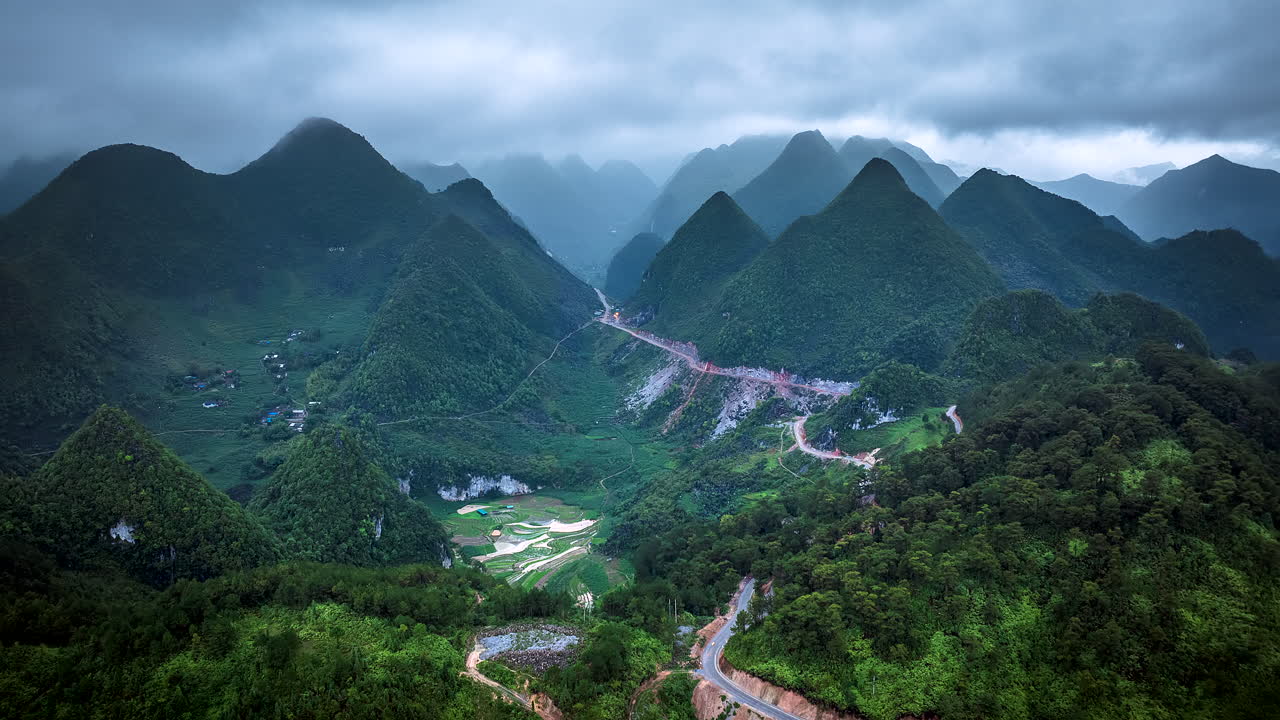 Ha Giang loop motorable road through mountain pass under rainy clouds, Natural scenery of Dong Van Karst Plateau, terraced rice fields and ethnic village, Aerial