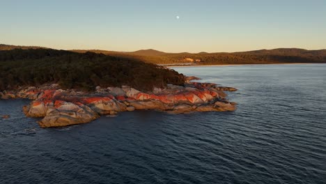 granite rocks along coast of bay of fires at sunset with full moon in the sky, tasmania in australia