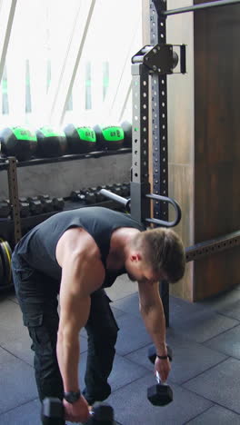 young sportsman in a modern gym. handsome athlete exercising with dumbbells. muscular bodybuilder actively training in luxury fitness club. vertical video